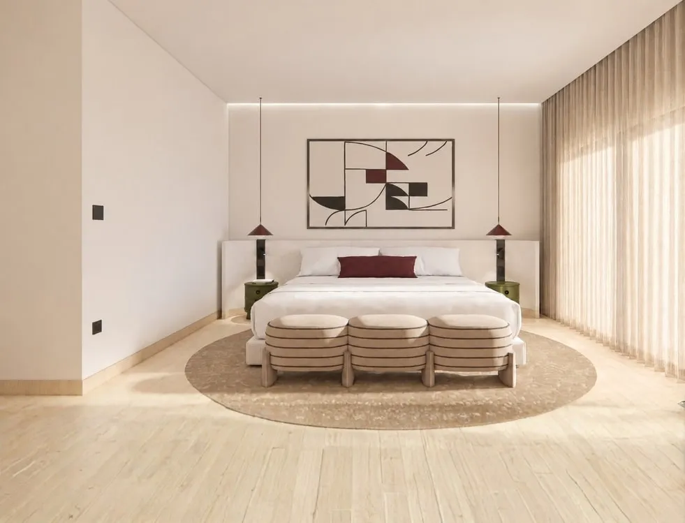 An Avani apartment bedroom in warm neutrals, with a round rug, a banded bench and full-height sheer curtains.